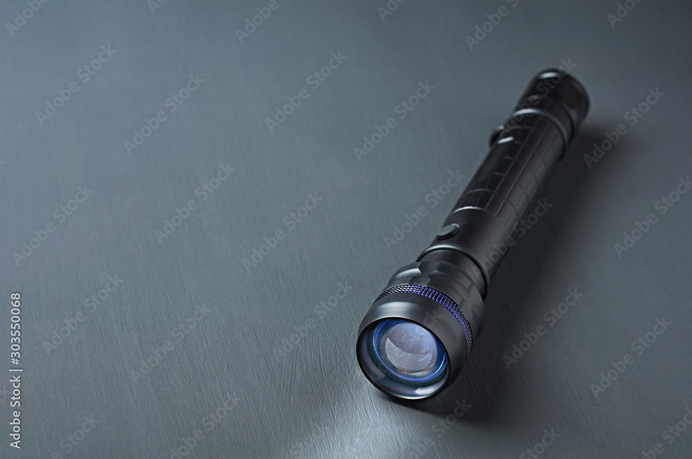 One black tactical flashlight lies on dark concrete table. Space for text One black tactical flashlight lies on dark concrete table. Space for text