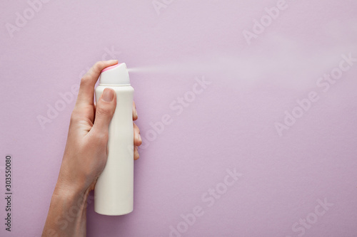 cropped view of woman spraying deodorant on violet background with white roses photo