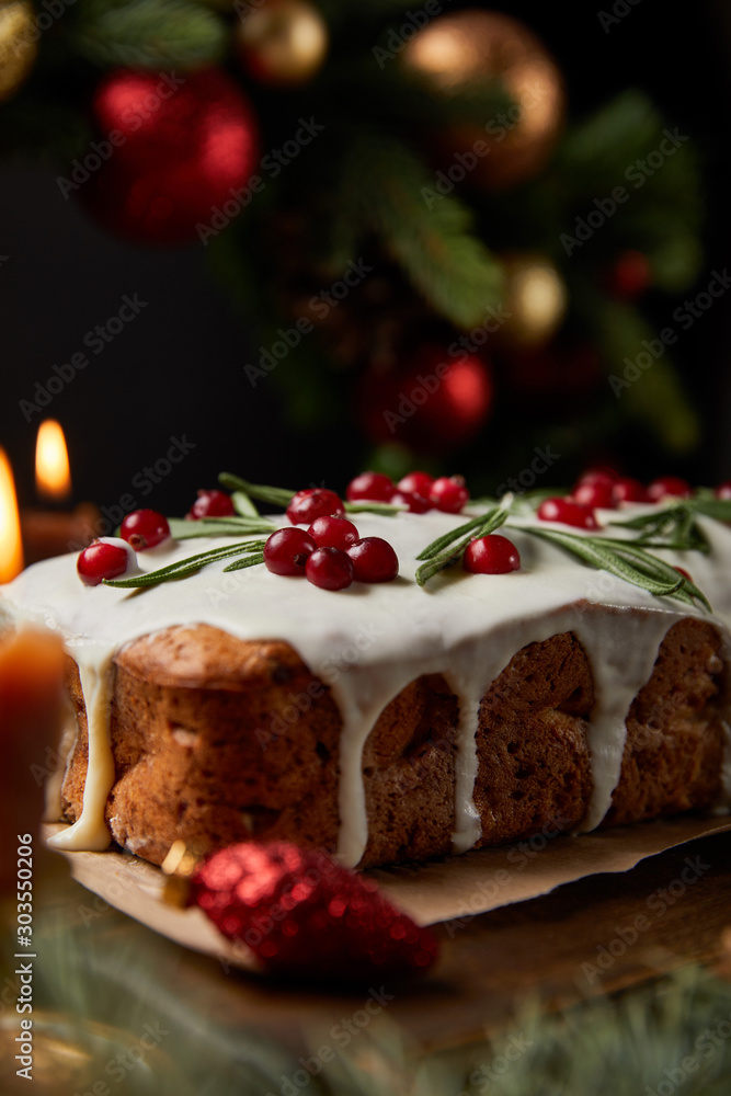 selective focus of traditional Christmas cake with cranberry near burning candles, Christmas wreath with baubles on wooden table selective focus of traditional Christmas cake with cranberry near burning candles, Christmas wreath with baubles on wooden table