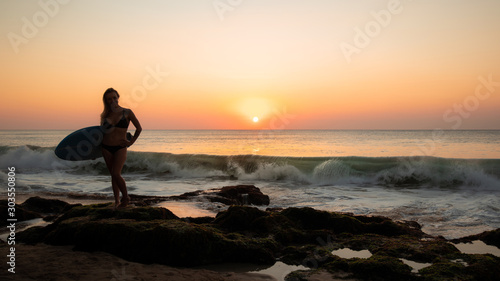 Silhouette of surfer girl with surfboard at the beach. Sunset time. Tegal Wangi beach, Bali, Indonesia