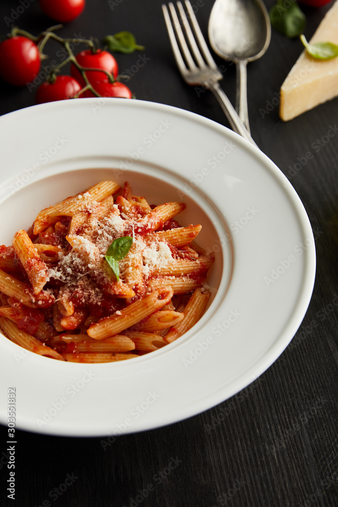 selective focus of tasty bolognese pasta with tomato sauce and Parmesan on white plate near ingredients and cutlery on black wooden background