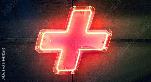 Illuminated red neon light, plus symbol on the wall photo