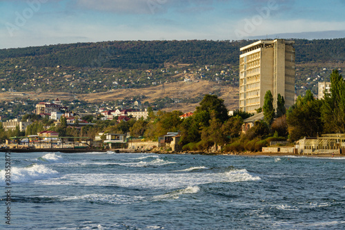 Feodosia, Crimea, Russia - September 26, 2019. View of hotels, health centers and residential buildings in city limits along Black Sea coast. In foreground is emerald water of Black Sea. photo