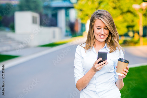 Young smart professional woman reading using phone. Female businesswoman reading news or texting sms on smartphone while drinking coffee on break from work.