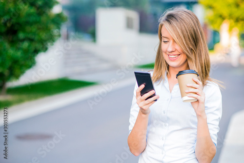Young smart professional woman reading using phone. Female businesswoman reading news or texting sms on smartphone while drinking coffee on break from work.