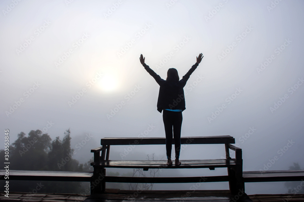 Φωτογραφία The image behind the women raise their arms on a wooden chair Background fog  and morning sunlight