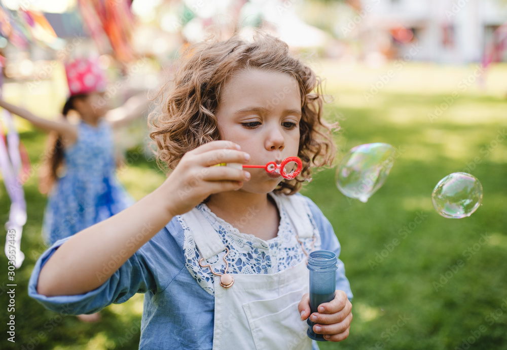 Small girl blowing bubbles outdoors in garden in summer.