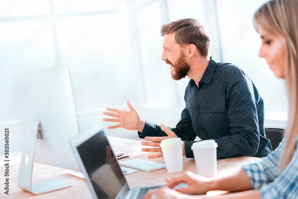 smiling businessman talking to a colleague sitting at his Desk