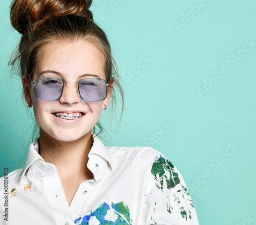 Young woman teenager girl with braces in white shirt with paint stains is smiling and winks on gray with copyspace photo