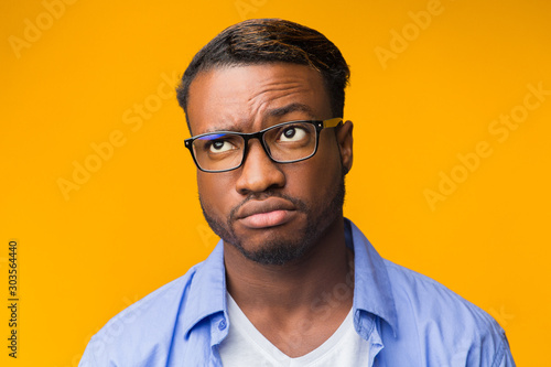 Fototapeta Naklejka Na Ścianę i Meble -  Puzzled African American Man Thinking About Something Standing, Orange Background