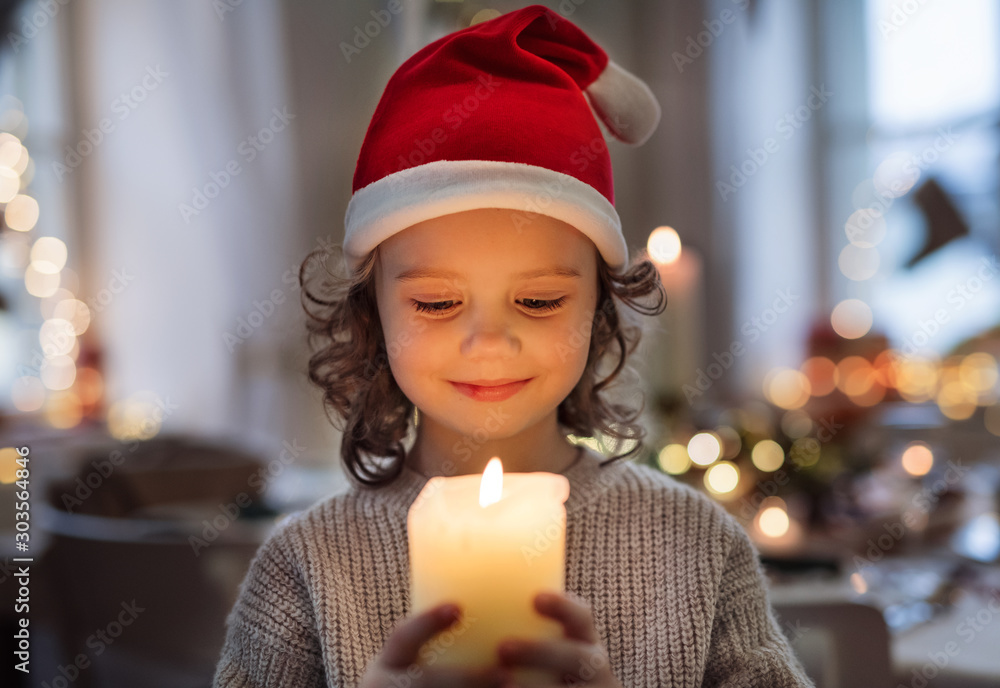 Cheerful small girl with santa hat indoors at Christmas, holding candle. - obrazy, fototapety, plakaty 