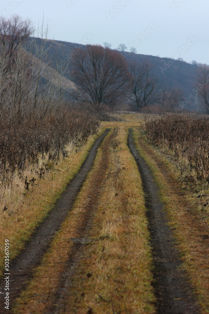 Fototapeta premium a dirt road stretching into the distance along the river Bank surrounded by hills