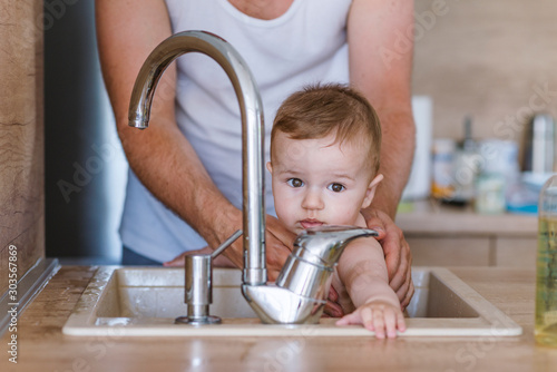 Cute snmiling baby taking bath in kitchen sink. Child playing with foam and soap bubbles in sunny kitchen, little boy bathing, fun with water photo