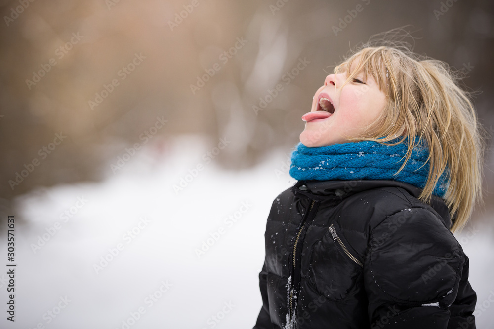 A cheerful child stands outside and catches snowflakes with his tongue on a cold winter day. Charming kid in a jacket with a blue scarf and blond hair is walking in the park. Activities for children A cheerful child stands outside and catches snowflakes with his tongue on a cold winter day. Charming kid in a jacket with a blue scarf and blond hair is walking in the park. Activities for children