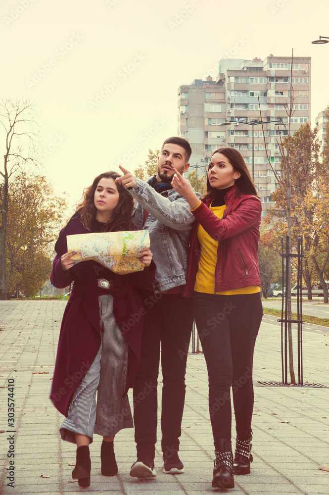 Naklejka premium three people city break tourists having adventures and fun, holding city map, urban outdoor autumn sightseeing and looking around