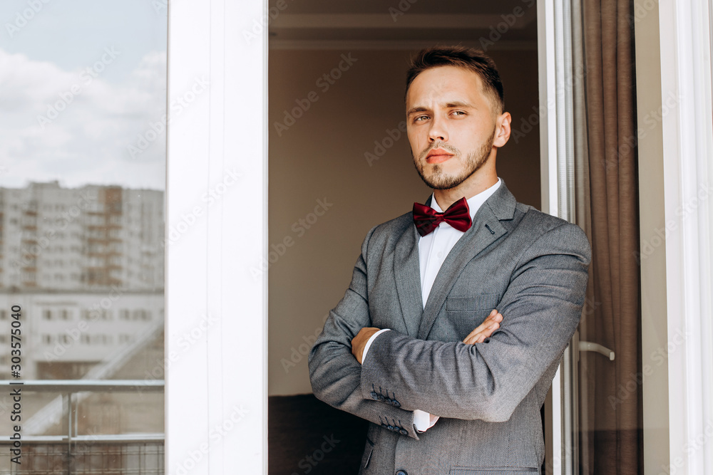 A serious groom in a gray suit standing by the window A serious groom in a gray suit standing by the window
