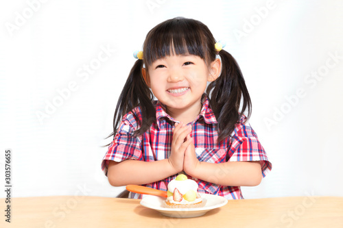 白背景でおやつのケーキを食べる前に「頂きます」をする幼い女の子。躾、マナー、行儀、幸せイメージ