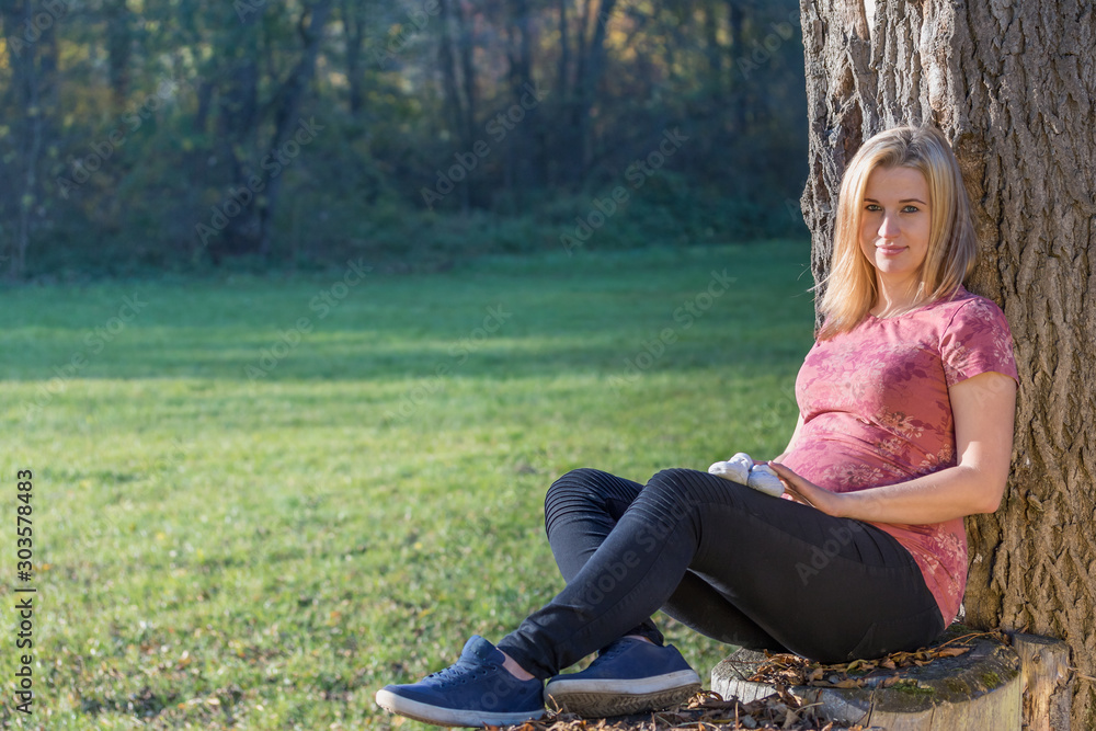 Portrait of young pregnant woman is sitting leaning against a tree in the park. Portrait of young pregnant woman is sitting leaning against a tree in the park.