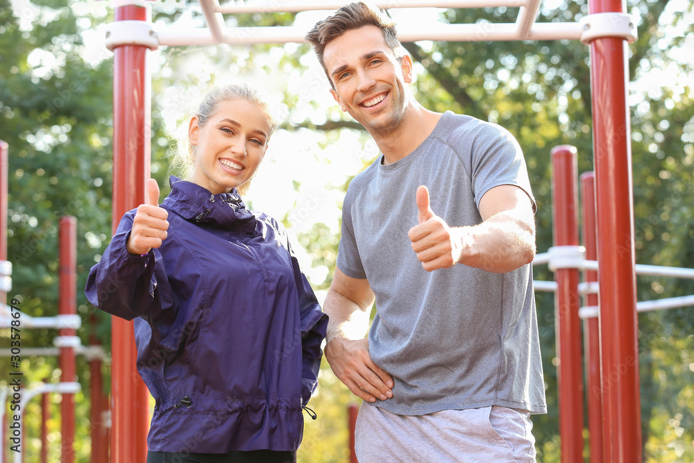 Obraz premium Sporty young couple showing thumb-up on athletic field