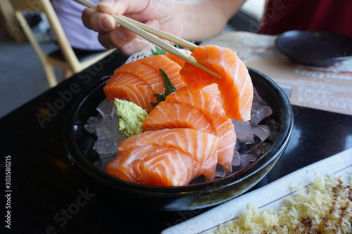 Man holding chopsticks eating fresh salmon sashimi on black blow. Japanese food in restaurant.