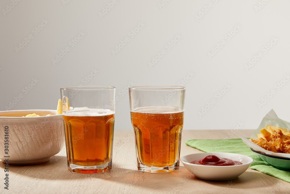 glasses of beer, chicken nuggets with french fries, ketchup and mayonnaise on wooden table on grey background glasses of beer, chicken nuggets with french fries, ketchup and mayonnaise on wooden table on grey background