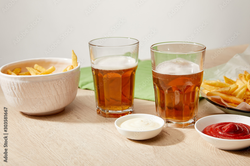 glasses of beer, chicken nuggets with french fries, ketchup and mayonnaise on wooden table on grey background glasses of beer, chicken nuggets with french fries, ketchup and mayonnaise on wooden table on grey background