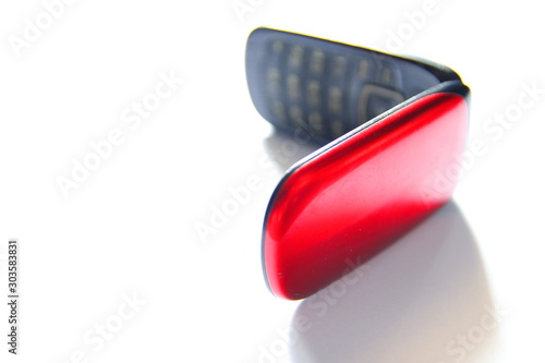 A classic folding mobile phone with buttons on a white background. Red cell shell-phone with a cover closing cover. 