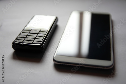 Retro cell phone next to a modern smartphone business. A business set of two phones. The glare on the screens of two phones.