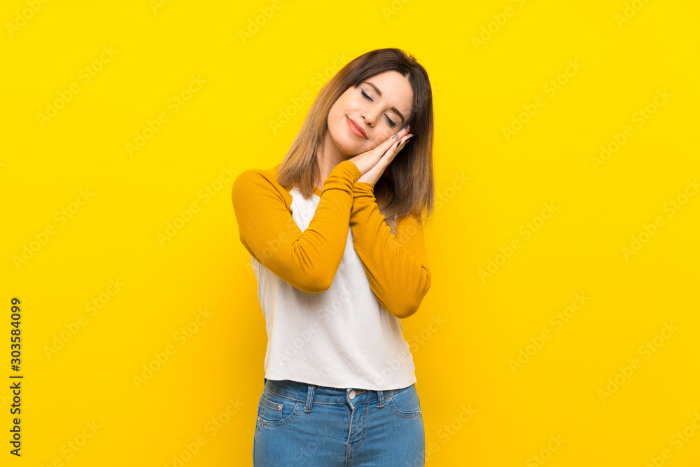 Pretty young woman over isolated yellow wall making sleep gesture in dorable expression Pretty young woman over isolated yellow wall making sleep gesture in dorable expression