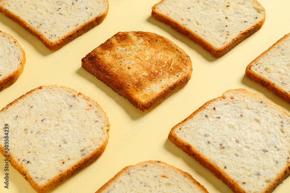 Toasted bread among fresh ones on color background. Concept of uniqueness
