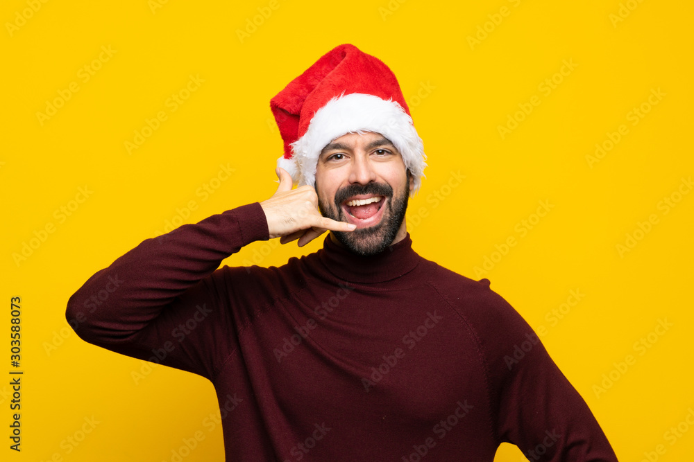 Man with christmas hat over isolated yellow background making phone gesture. Call me back sign Man with christmas hat over isolated yellow background making phone gesture. Call me back sign