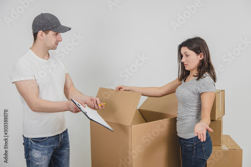 Young delivery guy transported all the cardboard boxes into new flat and is waiting for woman's signature, but she refuses to sign anything untill she check if everything is all right with her things. photo