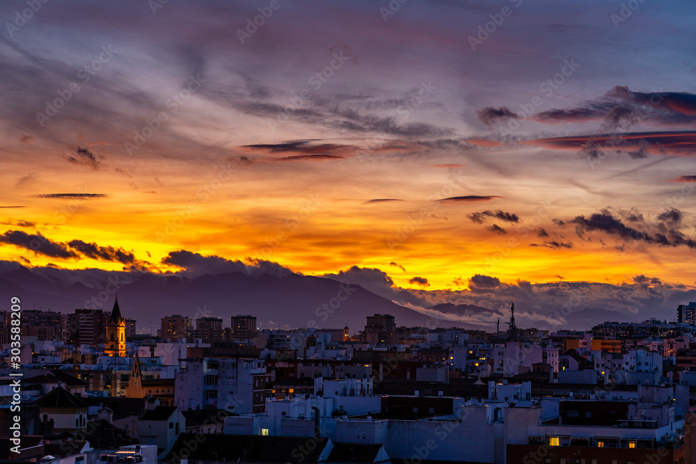 Blue hour view over Malaga, Spain - partly cloudy with yellow and red sky
