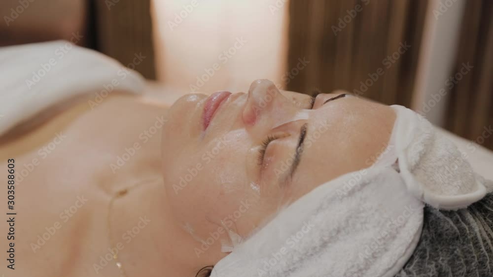 Woman lies on a couch with a transparent fabric anti-aging mask in a beauty salon. Woman lies on a couch with a transparent fabric anti-aging mask in a beauty salon.
