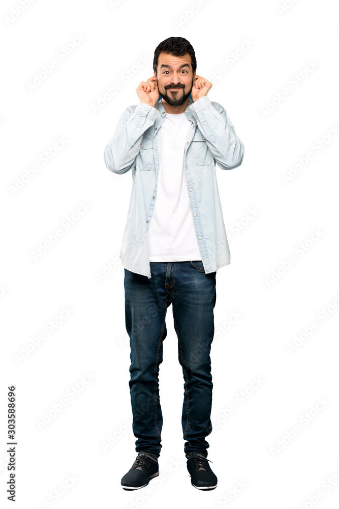Full-length shot of Handsome man with beard frustrated and covering ears over isolated white background Full-length shot of Handsome man with beard frustrated and covering ears over isolated white background