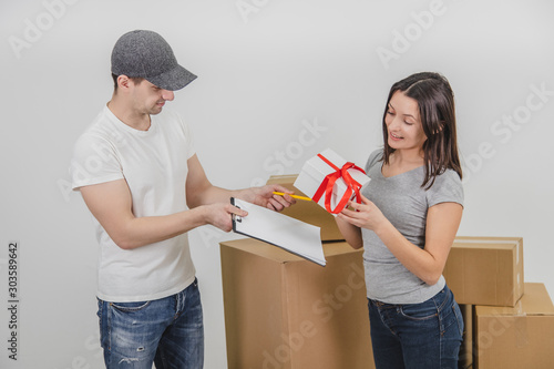 Courier delivered present for young woman who is moving into new apartment and wait for her signature. Woman is really happy.