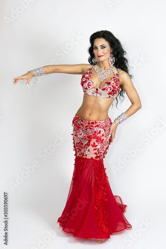 Brunette beautiful long red dress to perform belly dance on a white background