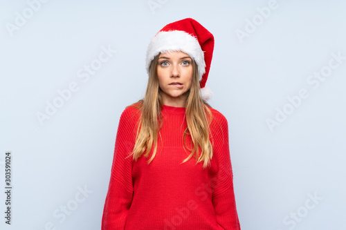 Girl with christmas hat over isolated blue background having doubts and with confuse face expression