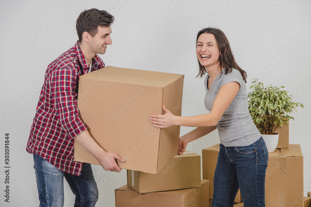 Couple in a new flat. Young man is totaly exhausted. He can not hold heavy box anymore, he almost dropped it, but woman helped him. Couple in a new flat. Young man is totaly exhausted. He can not hold heavy box anymore, he almost dropped it, but woman helped him.