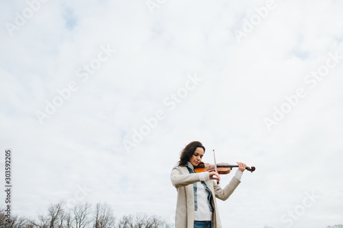 Beautiful woman in a coat playing violin under a sky with her eyes closed photo