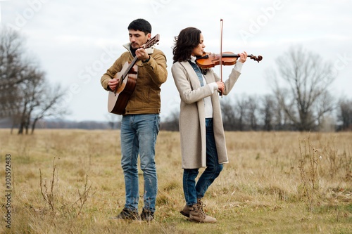 Violinist and guitarist playing music in the middle of anl autumn field of grass photo