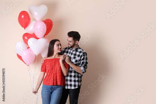 Beautiful couple with heart shaped balloons on beige background, space for text. Valentine's day celebration