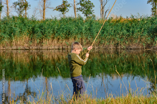 A boy holds a fishing rod over the water for fishing.