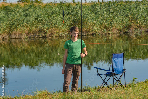 A young man stands with a fishing rod on the river bank for fishing.