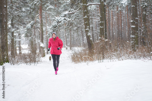 Smiling woman jogging in winter forest with dog