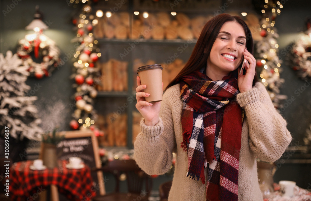 Beautiful woman with cup of coffee talking on mobile phone in decorated cafe. Christmas celebration Beautiful woman with cup of coffee talking on mobile phone in decorated cafe. Christmas celebration