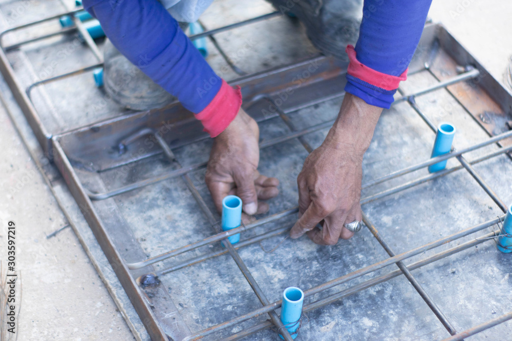 Workers are using steel pliers to clamp the wire in order to twist to fasten the blue PVC tube strand to the steel frame laid for making a pattern for making cement pipe caps. Workers are using steel pliers to clamp the wire in order to twist to fasten the blue PVC tube strand to the steel frame laid for making a pattern for making cement pipe caps.