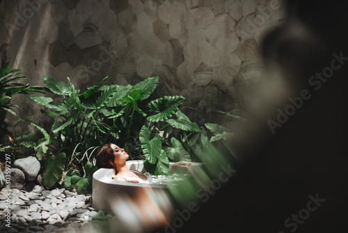 Woman relaxing in round outdoor bath with tropical flowers, organic skin care, luxury spa hotel, lifestyle photo