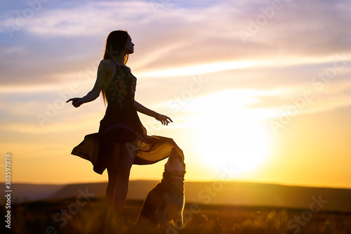Beautiful young girl in a light flying dress at sunset in the mountains with a husky dog. A warm sunset light illuminates and falls on a girl and her dog