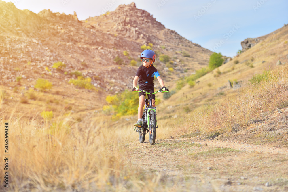 Fototapeta premium Happy kid boy of 7 years having fun in autumn park with a bicycle on beautiful fall day. Active child wearing bike helmet